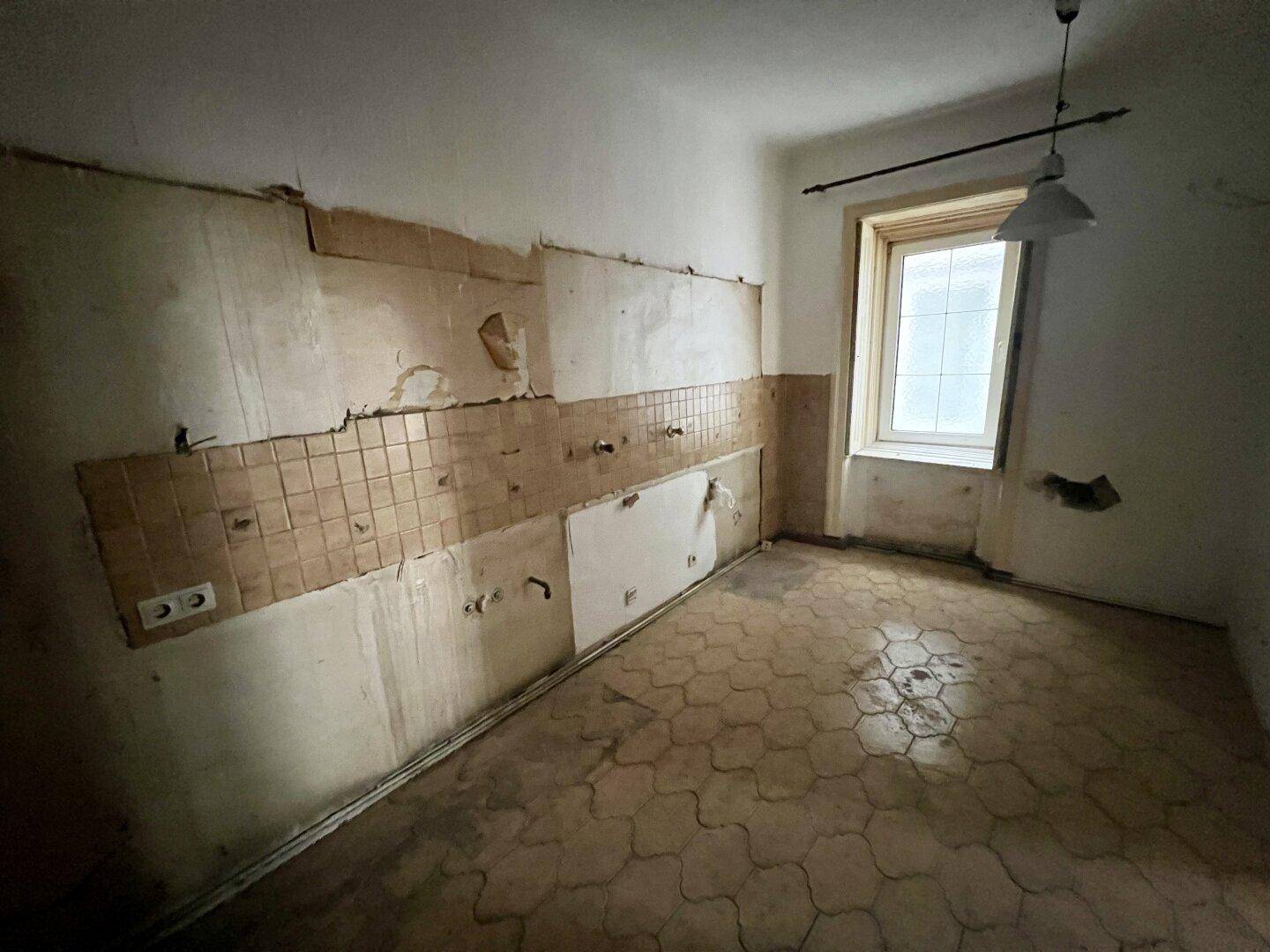 Renovierungsbedürftige Küche mit alten Wand- und Bodenfliesen sowie einem Fenster.