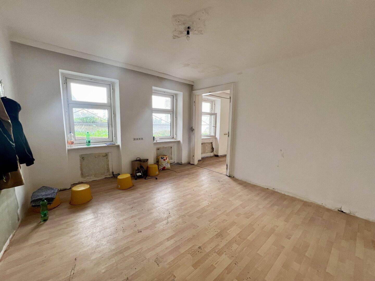 Leerer Raum mit Holzboden und zwei Fenstern, bereit für die Renovierung und Gestaltung.