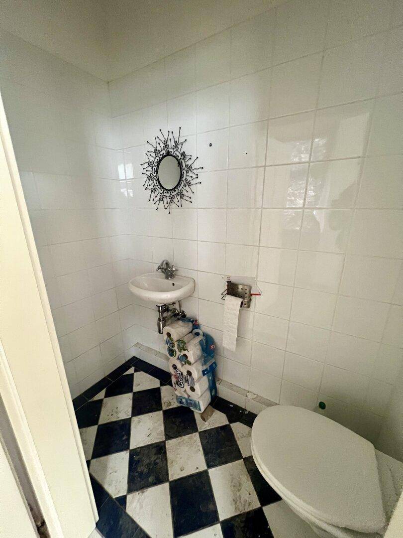 Kleines Gäste-WC mit schwarz-weiß kariertem Boden, weißen Wandfliesen und Waschbecken.