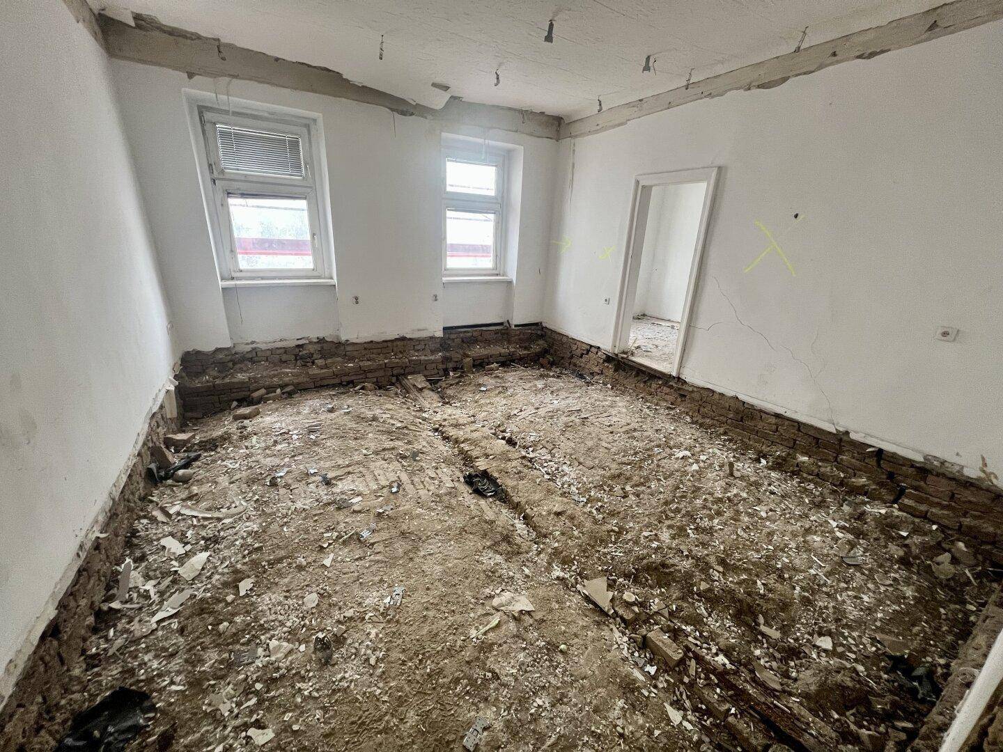 Zimmer im Rohzustand mit freigelegten Wänden und Boden, bereit für eine umfassende Renovierung.