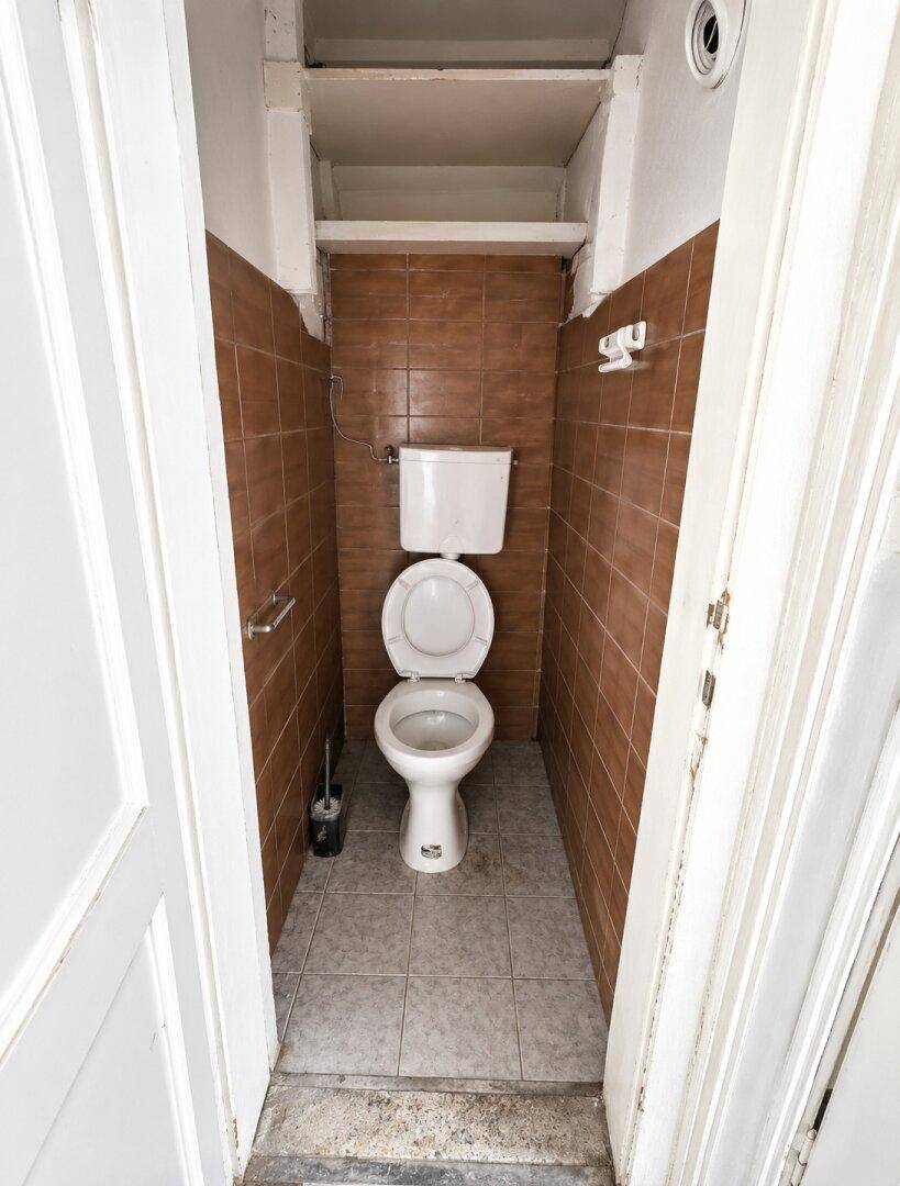 Schmales WC mit braunen Wandfliesen und einer einfachen Toilette.