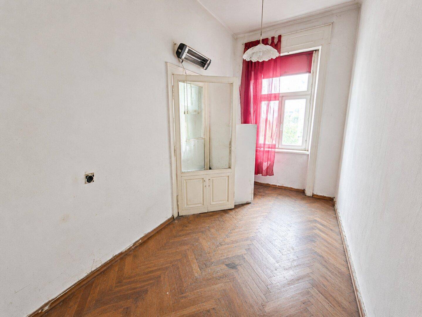 Zimmer mit Fischgrätparkett, roten Vorhängen und einer alten Glastür.