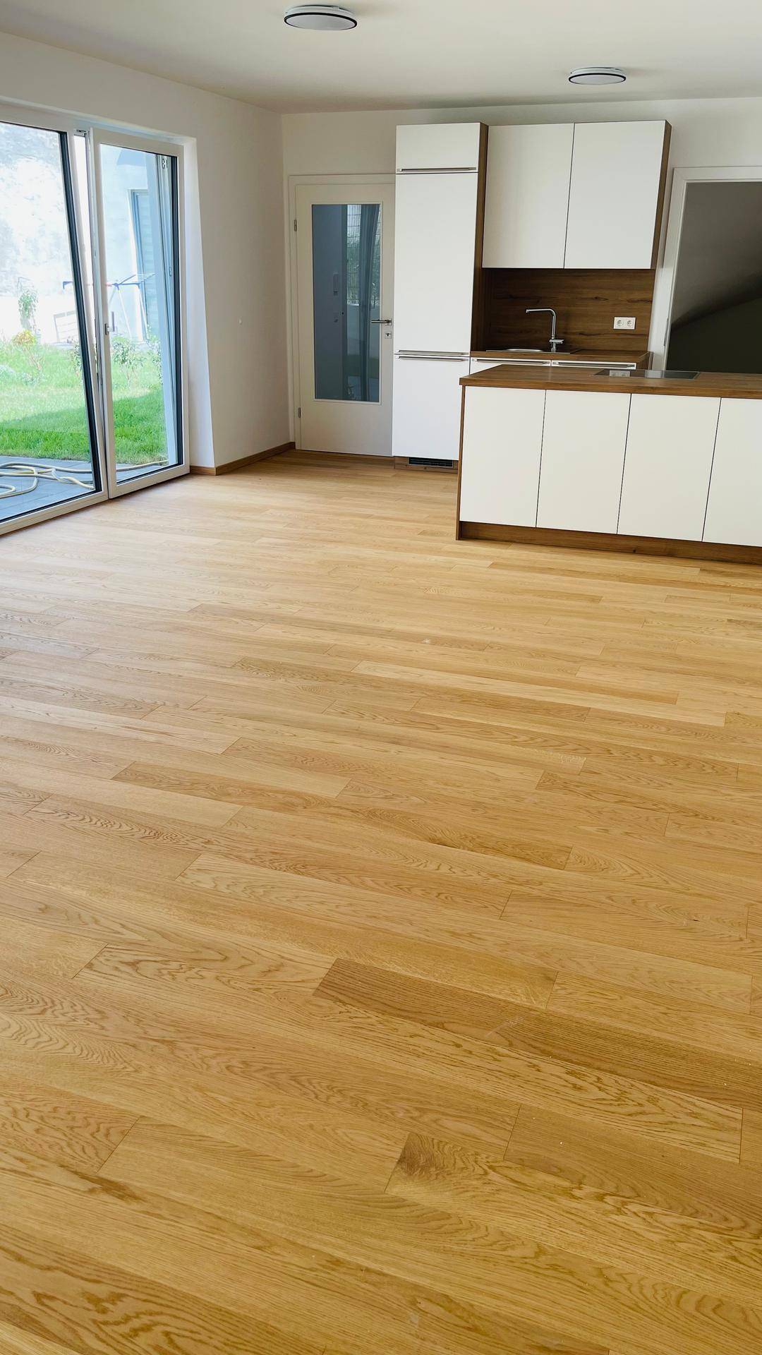 Heller offener Wohnbereich mit moderner Küche, Holzboden und direktem Zugang zum Garten.