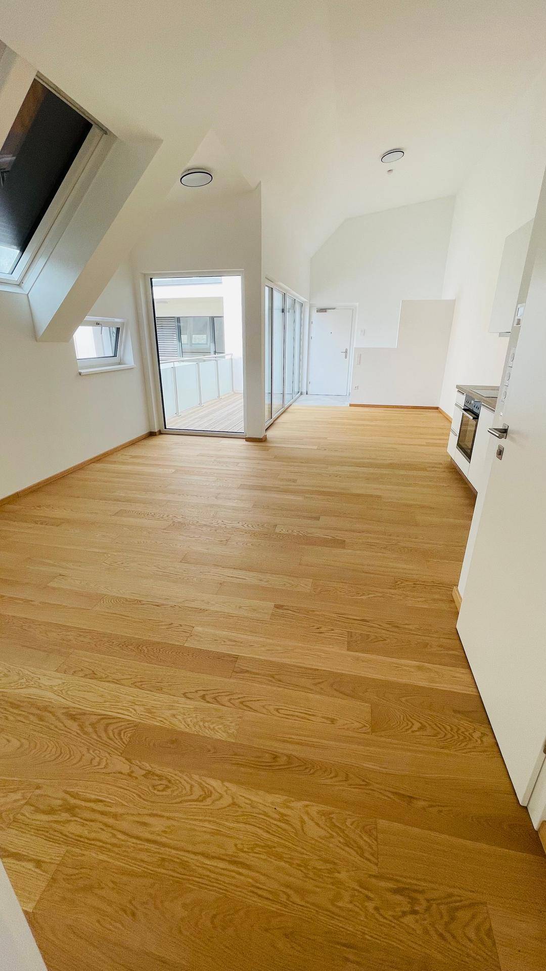 Offener Wohnbereich mit Holzboden, Dachschrägen und großen Fenstern, die viel Licht hereinlassen.