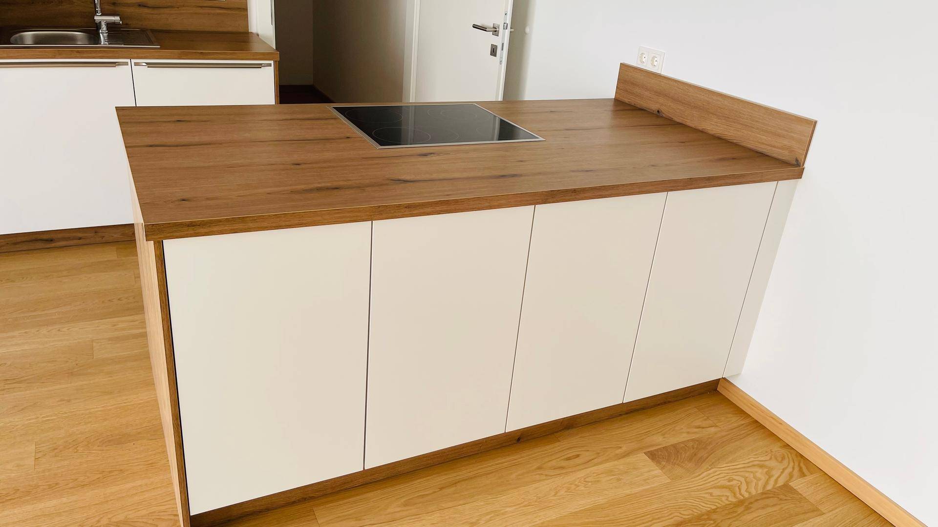 Moderne Kücheninsel mit Induktionskochfeld und Holz-Arbeitsplatte, umgeben von hellem Holzboden.