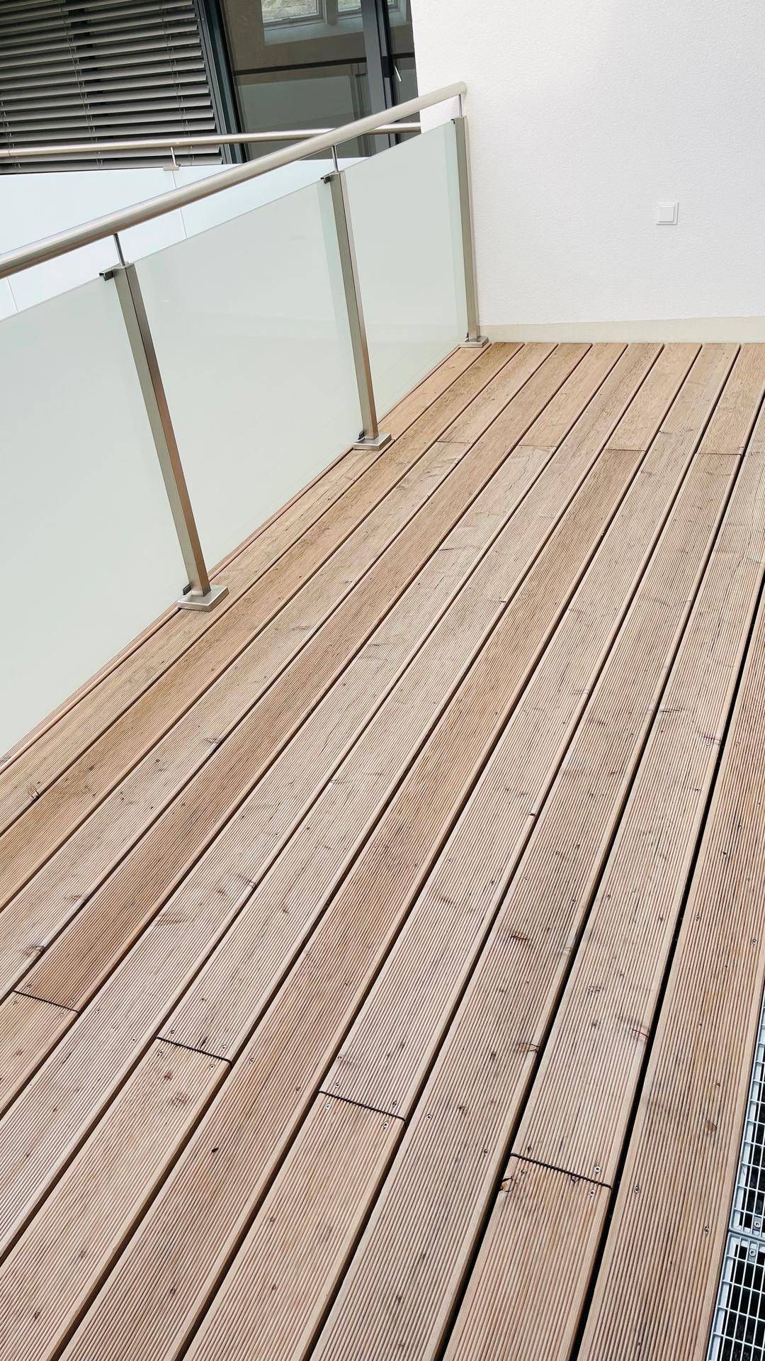 Geräumiger Balkon mit Holzdielen und eleganten Glasgeländern, perfekt für sonnige Stunden im Freien.
