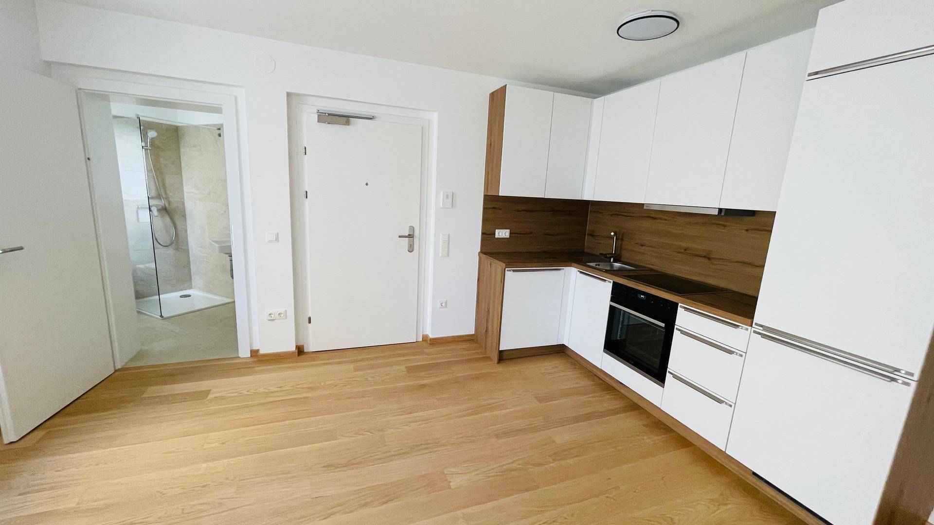 Heller Wohnbereich mit Holzboden und integrierter Küchenzeile, angrenzend an ein modernes Badezimmer.