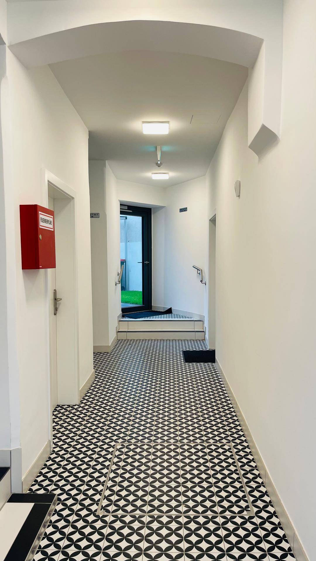 Heller Flur mit auffälligen schwarz-weißen Fliesen und einem roten Briefkasten an der Wand.