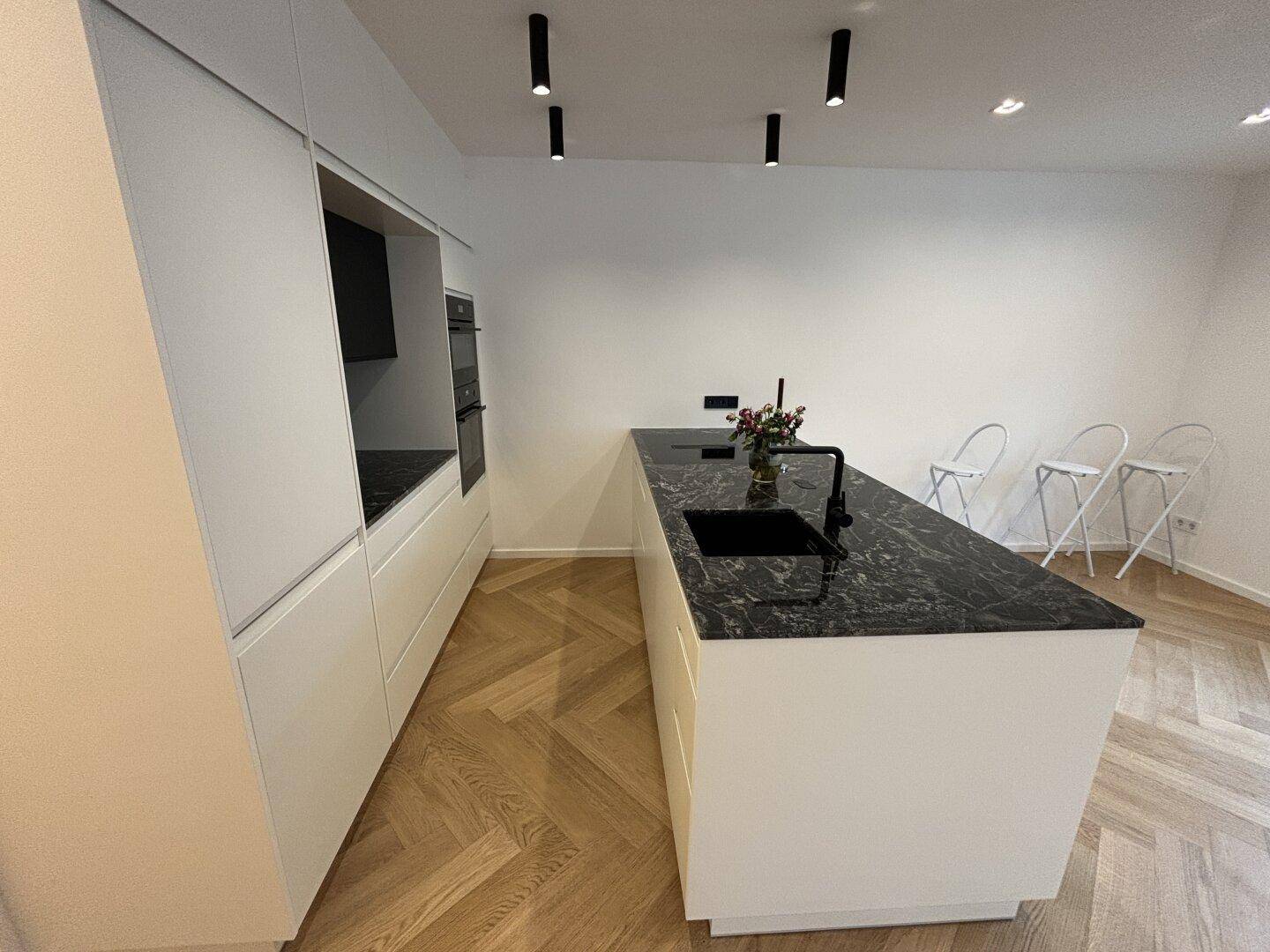 Elegante Küche mit schwarzer Granit-Arbeitsplatte, integrierten Geräten und weißer Front.
