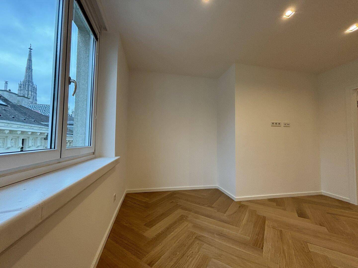 Helles Zimmer mit Fischgrätparkett und Blick auf die Stadt mit Kirchturmspitze.
