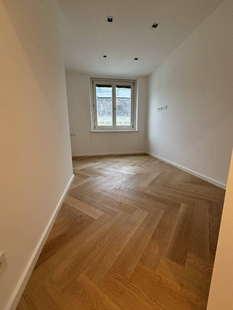 Ruhiges Zimmer mit Fischgrätparkett und einem Fenster, das viel Tageslicht hereinlässt.