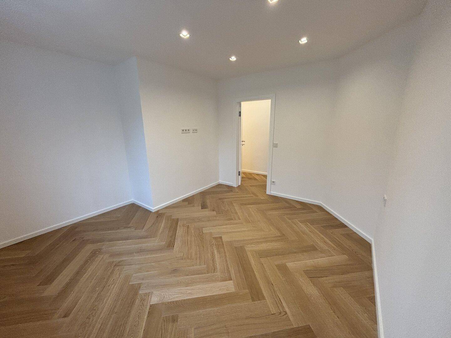 Geräumiges Zimmer mit Fischgrätparkett und Zugang zu einem weiteren Raum.