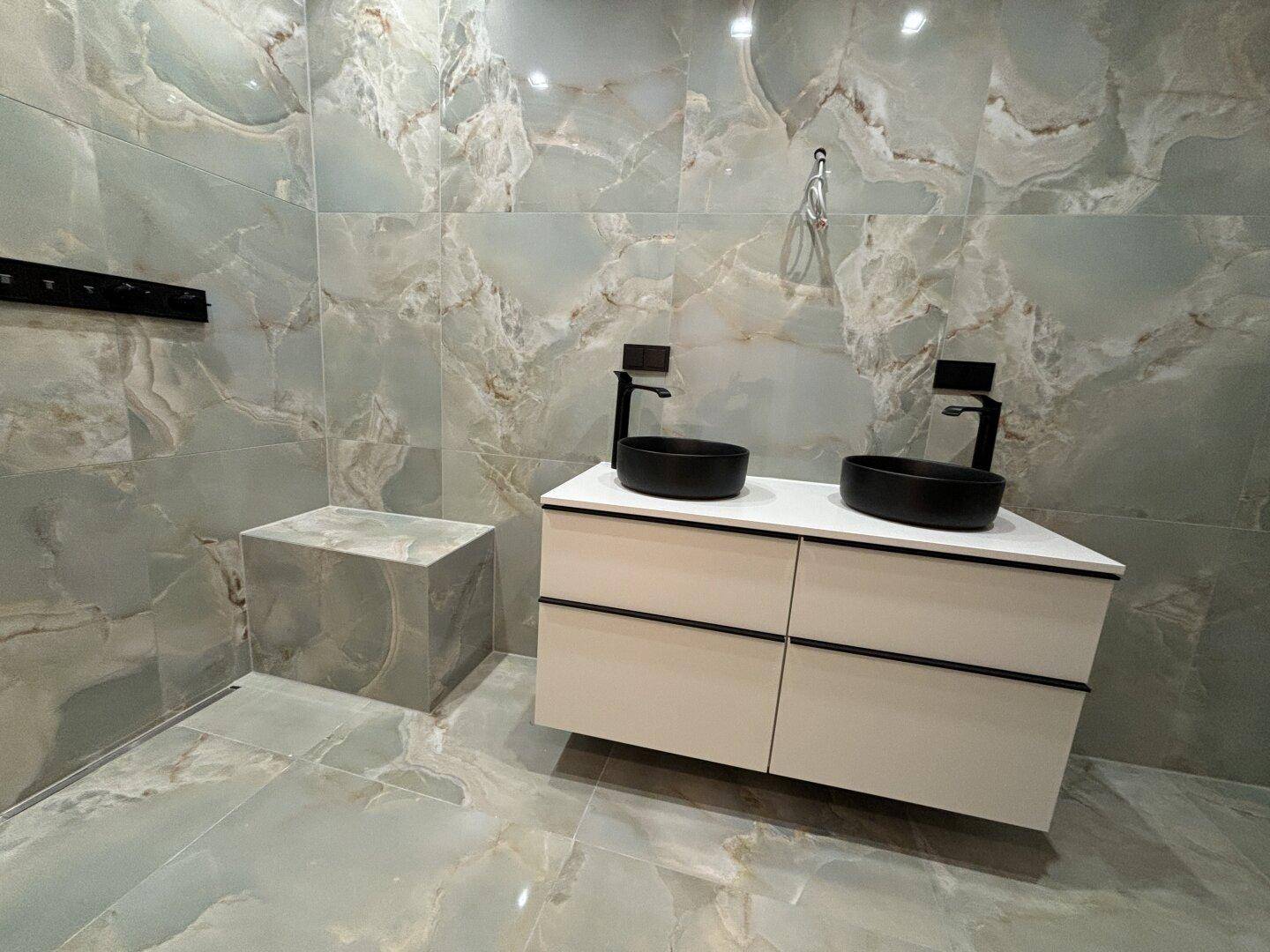 Modernes Badezimmer mit doppelten Waschbecken, schwarzen Armaturen und großformatigen Fliesen.