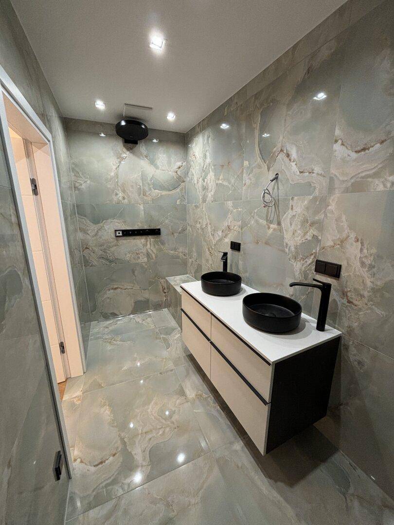 Elegantes Badezimmer mit doppelten Aufsatzwaschbecken, schwarzen Armaturen und Marmorfliesen.