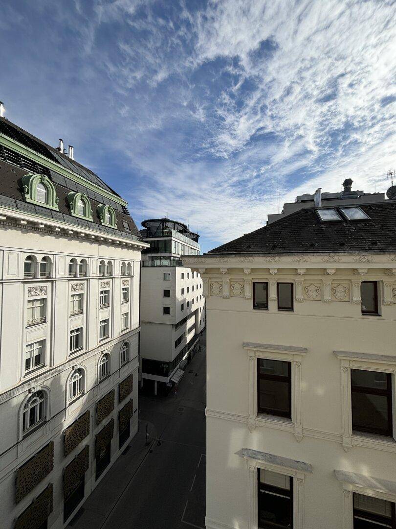 Blick auf eine belebte Stadtstraße mit historischen und modernen Gebäuden unter blauem Himmel.