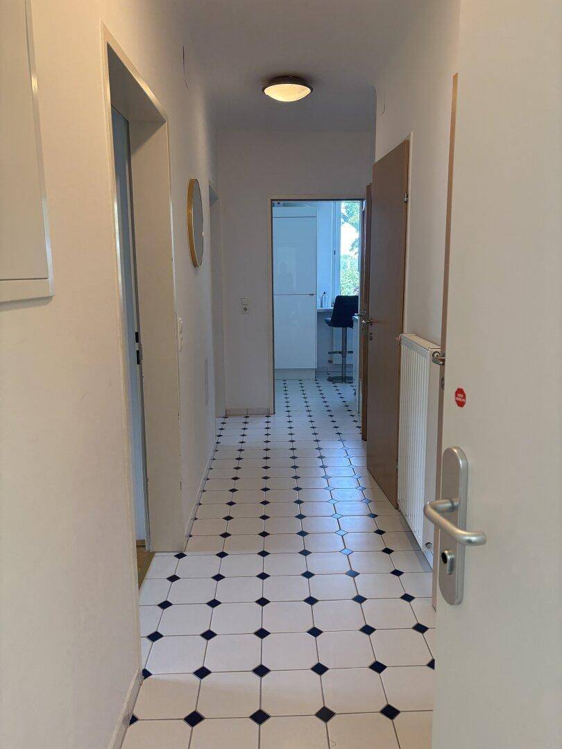 Langer Flur mit schwarz-weiß gefliestem Boden und Türen zu verschiedenen Räumen.