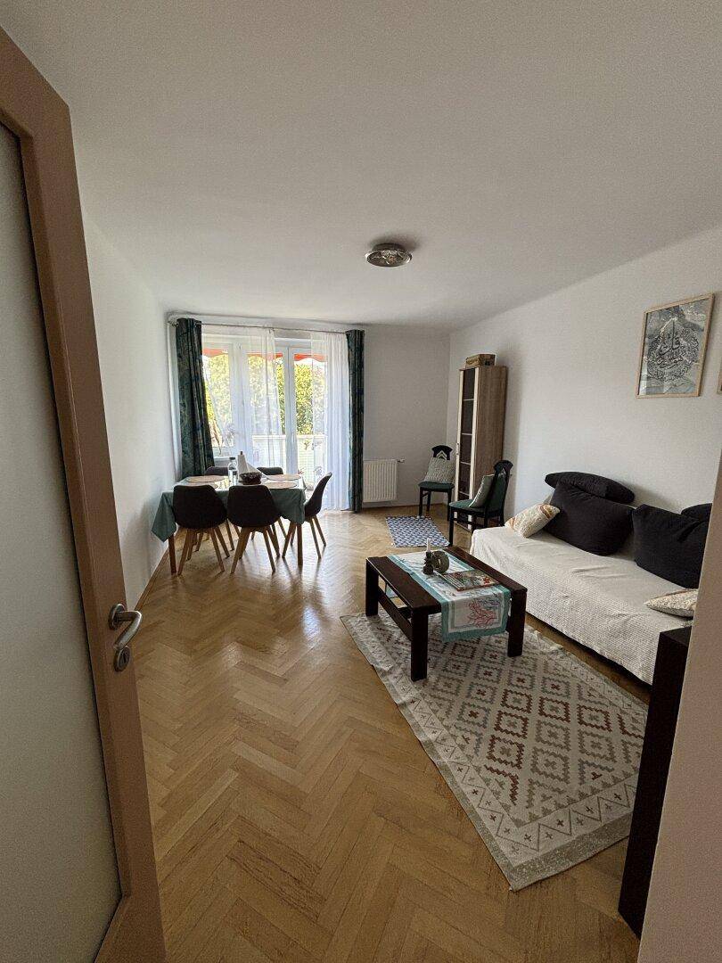 Heller Wohn- und Essbereich mit Fischgrätparkett, Sofa und Esstisch.