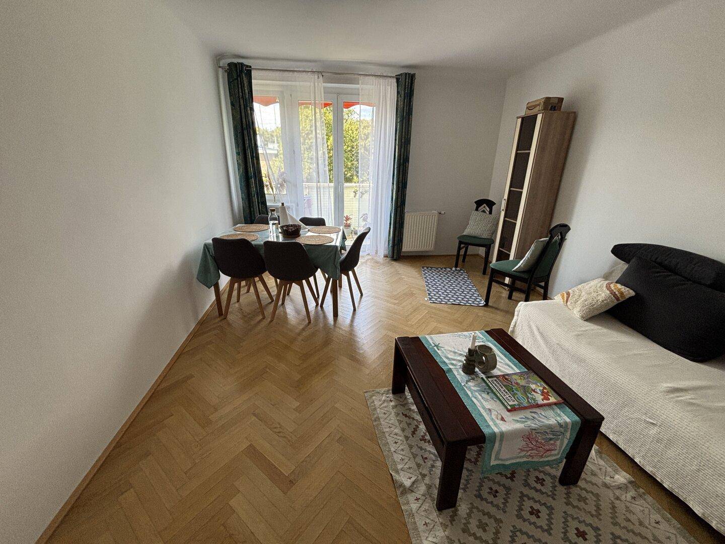 Geräumiger Wohn- und Essbereich mit Holzparkett und Zugang zu einem Balkon.