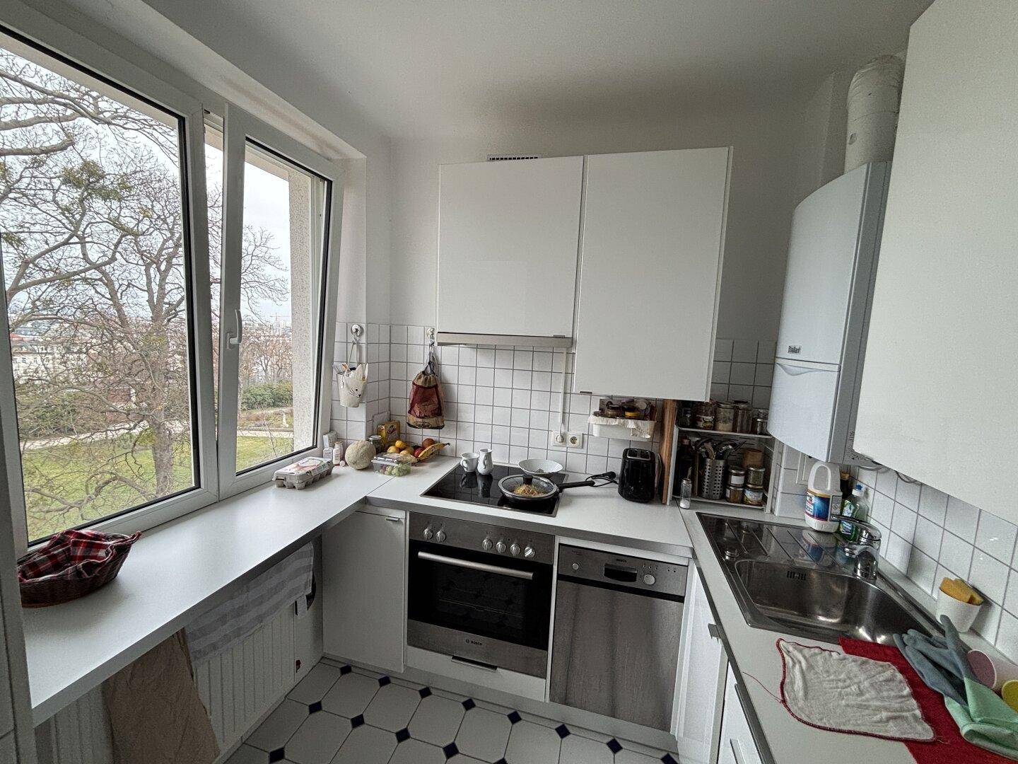 Funktionale Küche mit weißen Schränken, Fliesen und einem großen Fenster mit Blick ins Grüne.