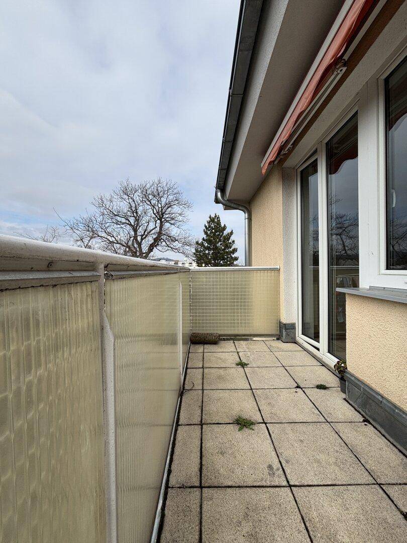 Balkon mit Fliesenboden und Blick auf kahle Bäume unter bewölktem Himmel.
