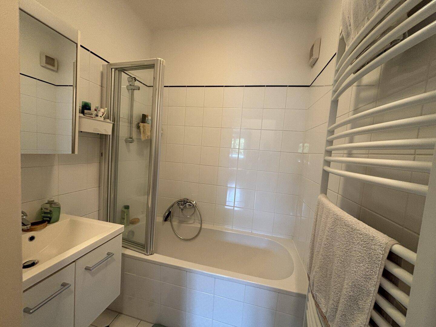 Helles Badezimmer mit Badewanne, Duschabtrennung, Waschbecken und Handtuchheizkörper.