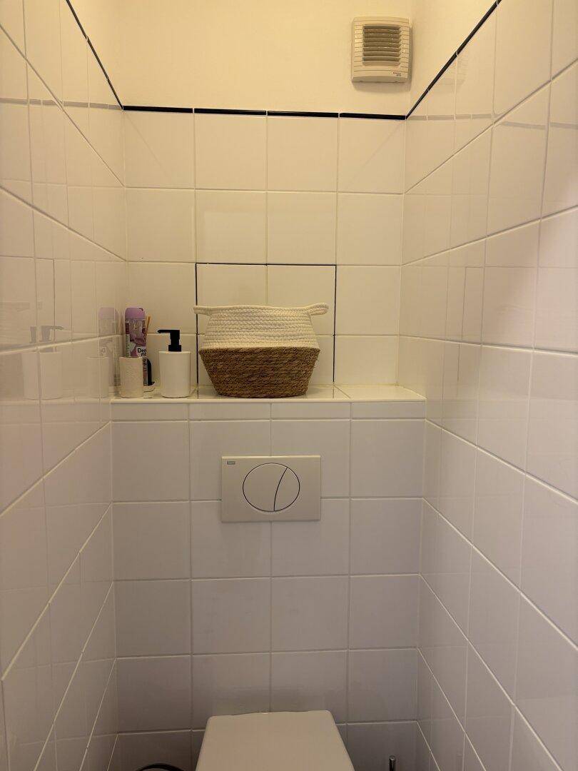 Separate Toilette mit weißen Fliesen und Wand-WC in einem kleinen Raum.