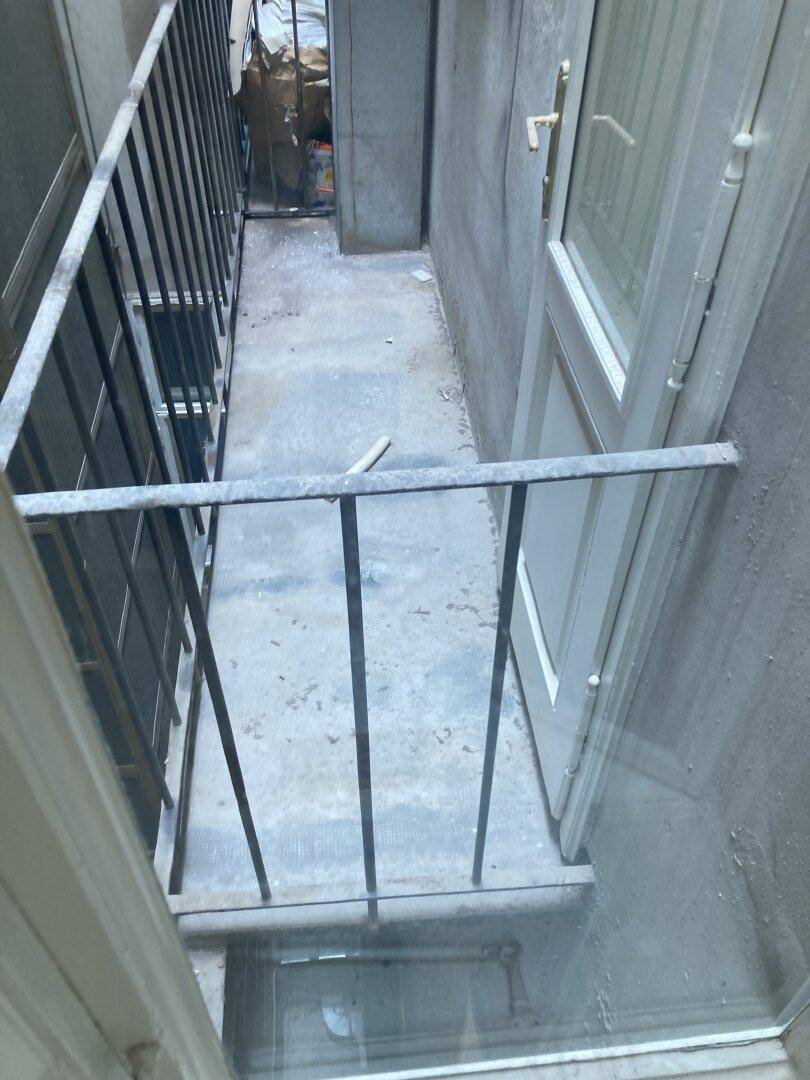 Schmaler Balkon mit Metallgeländer und Blick auf einen Innenhof, zugänglich durch eine Tür.