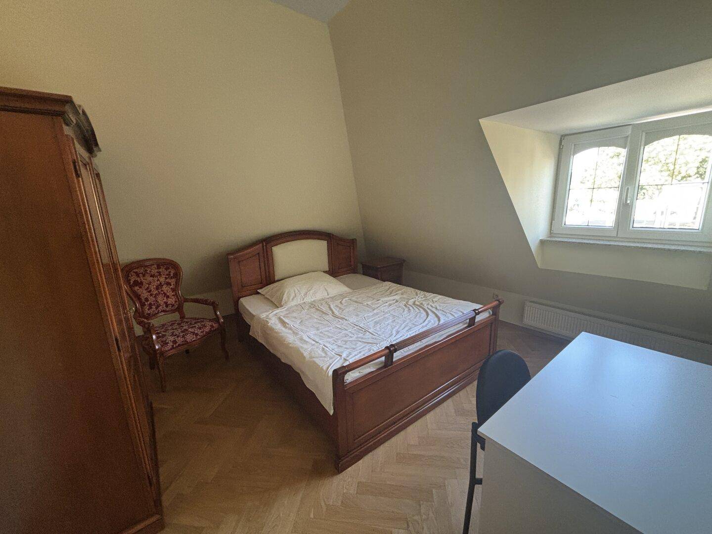 Helles Schlafzimmer im Dachgeschoss mit Bett, Schreibtisch und Fenster unter der Dachschräge.