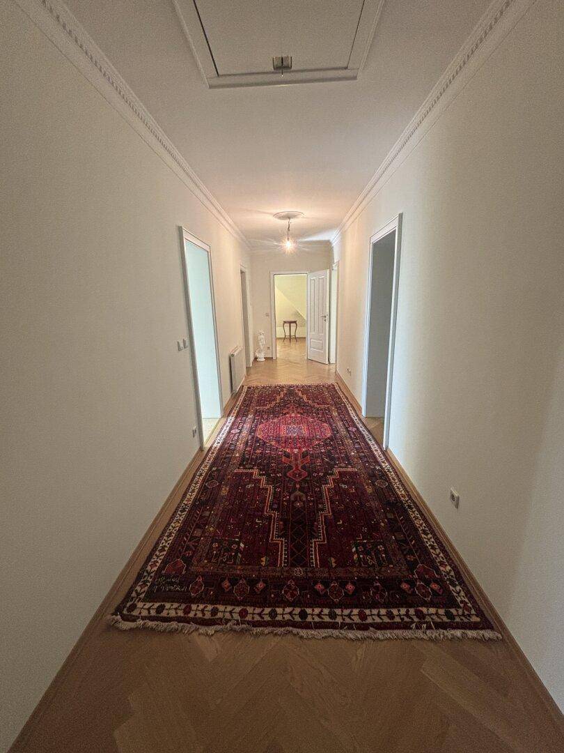 Langer Flur mit Fischgrätparkett und einem traditionellen Teppich, der zu verschiedenen Zimmern führt.