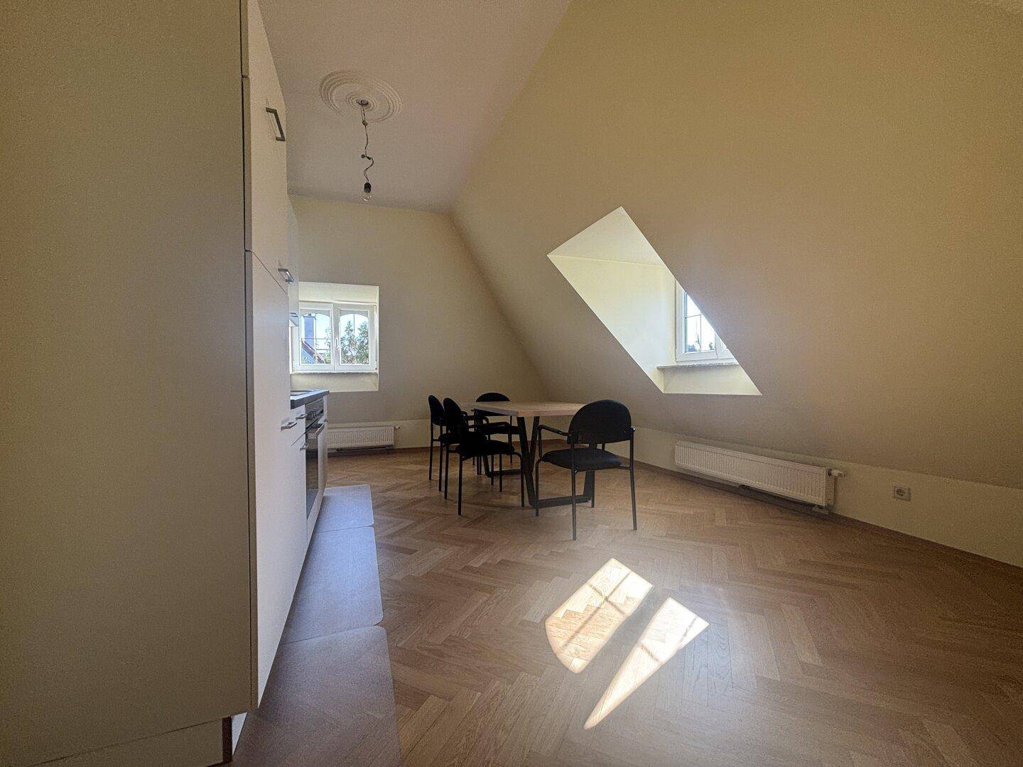 Offener Küchen- und Essbereich im Dachgeschoss mit weißen Schränken und viel Tageslicht durch Dachfenster.