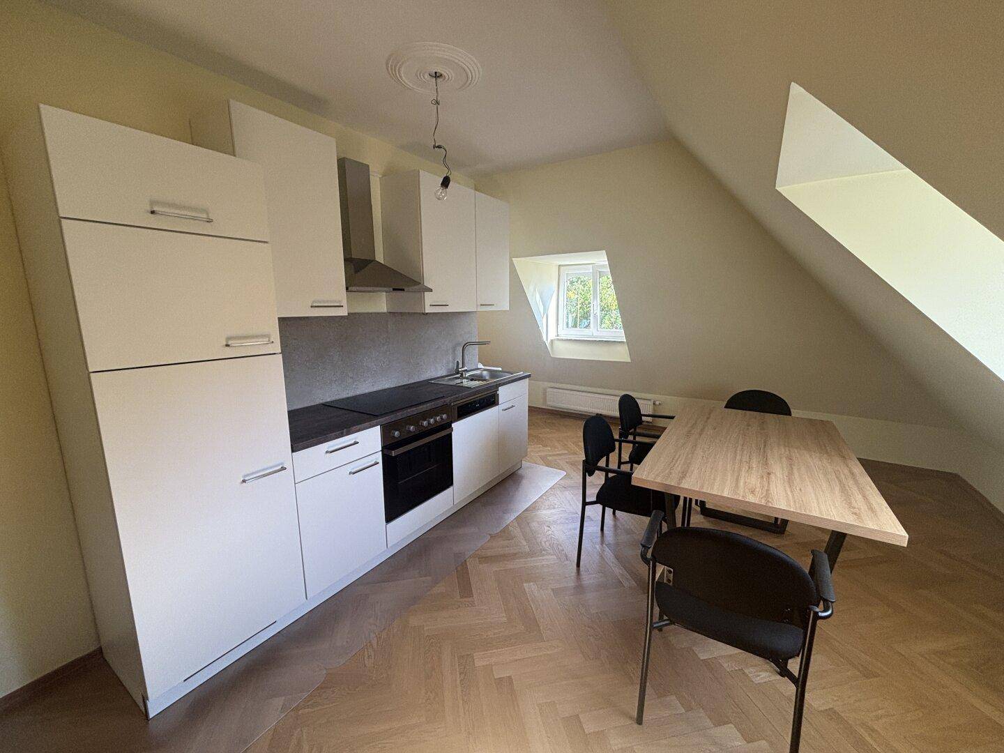 Moderne Küche in einer Dachgeschosswohnung mit weißen Schränken, Esstisch und schrägen Decken.