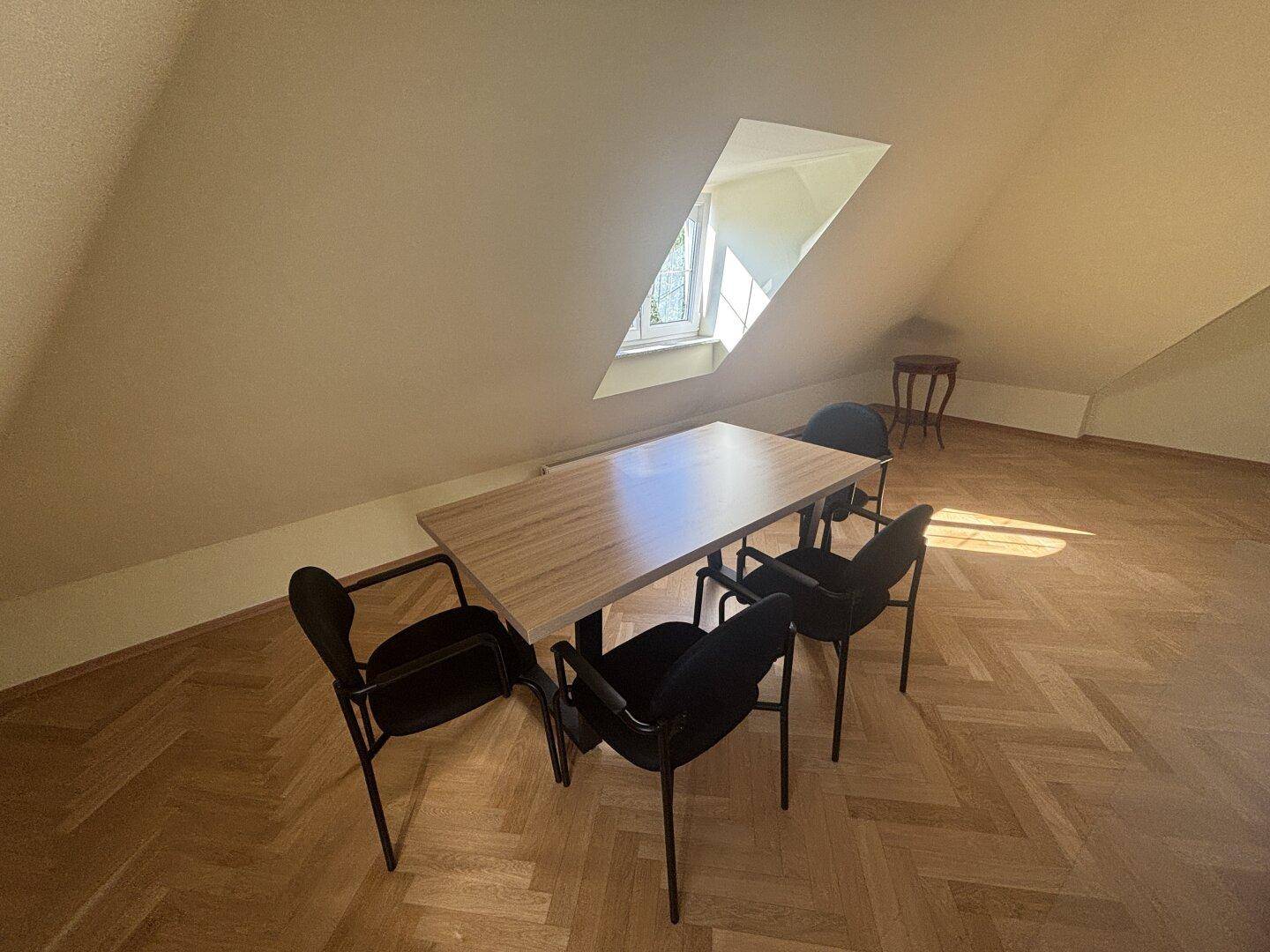 Heller Essbereich im Dachgeschoss mit Holztisch, schwarzen Stühlen und Fischgrätparkett unter der Dachschräge.