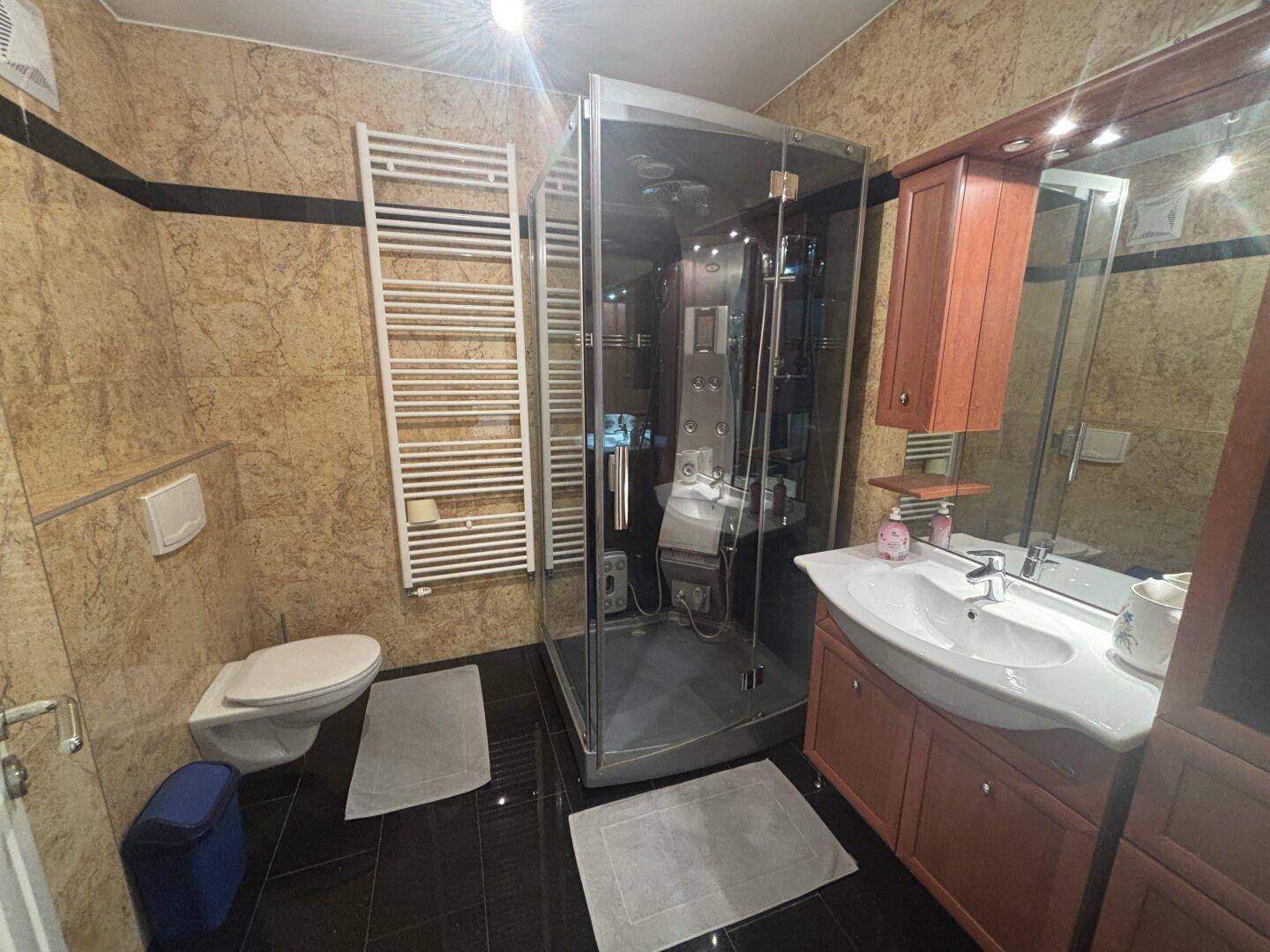 Funktionales Badezimmer mit gemusterten Fliesen, Duschkabine, WC und beheiztem Handtuchhalter.