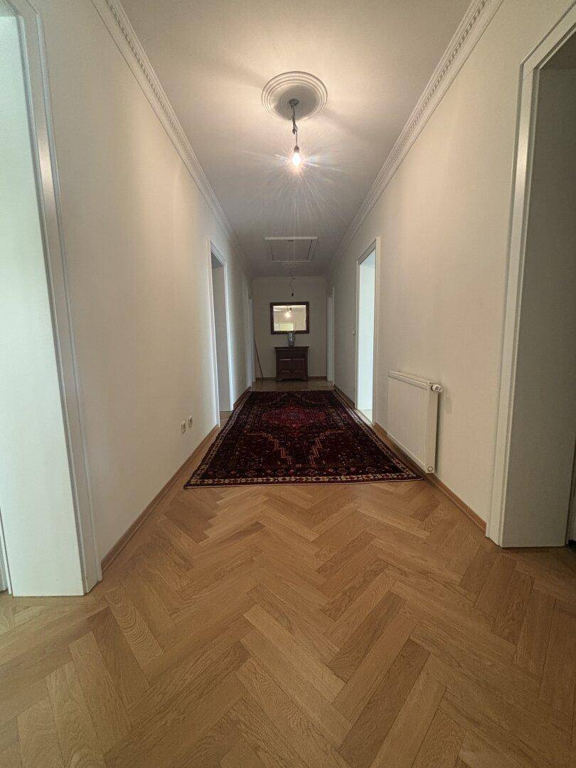 Heller Flur mit Fischgrätparkett und einem langen Teppich, der den Raum optisch verlängert.