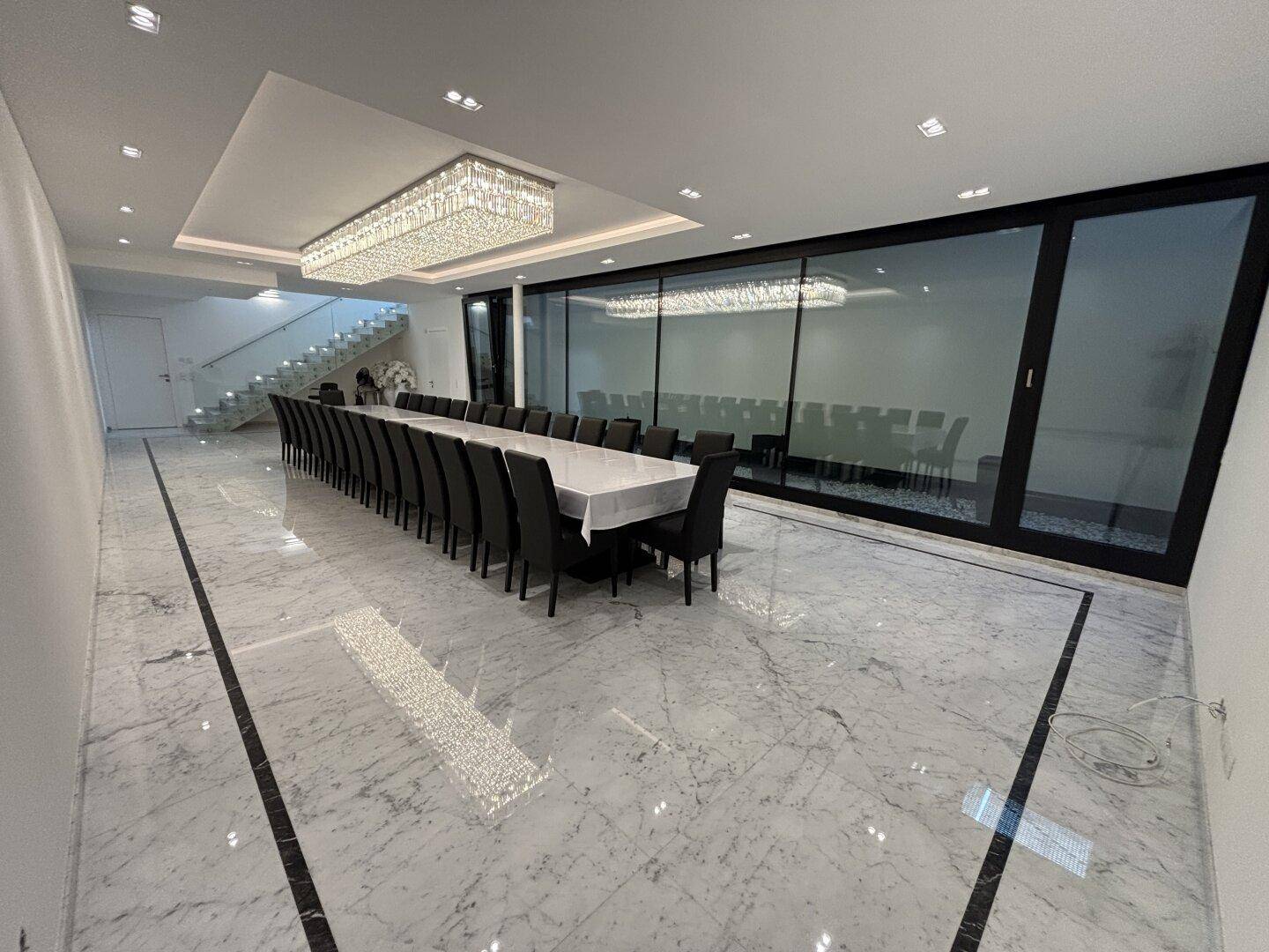 Geräumiger Speisesaal mit poliertem Marmorboden, langer Tafel und moderner Deckenbeleuchtung.
