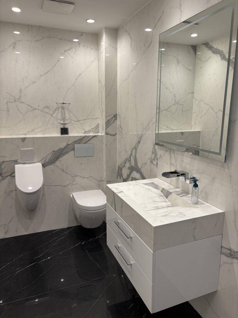 Modernes Badezimmer mit Marmorwänden, schwarzem Fliesenboden, schwebendem Waschtisch und Urinal.