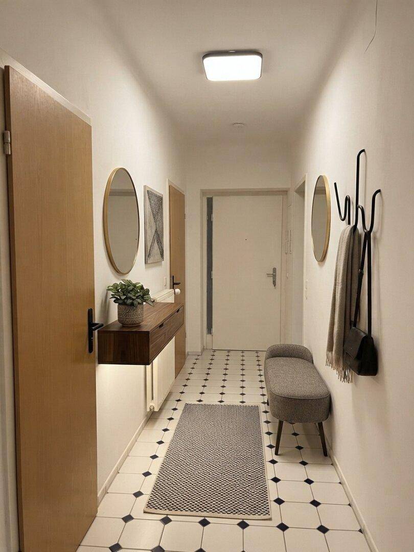 Heller Flur mit gemusterten Fliesen, schwebender Konsole, Garderobe und Sitzbank.