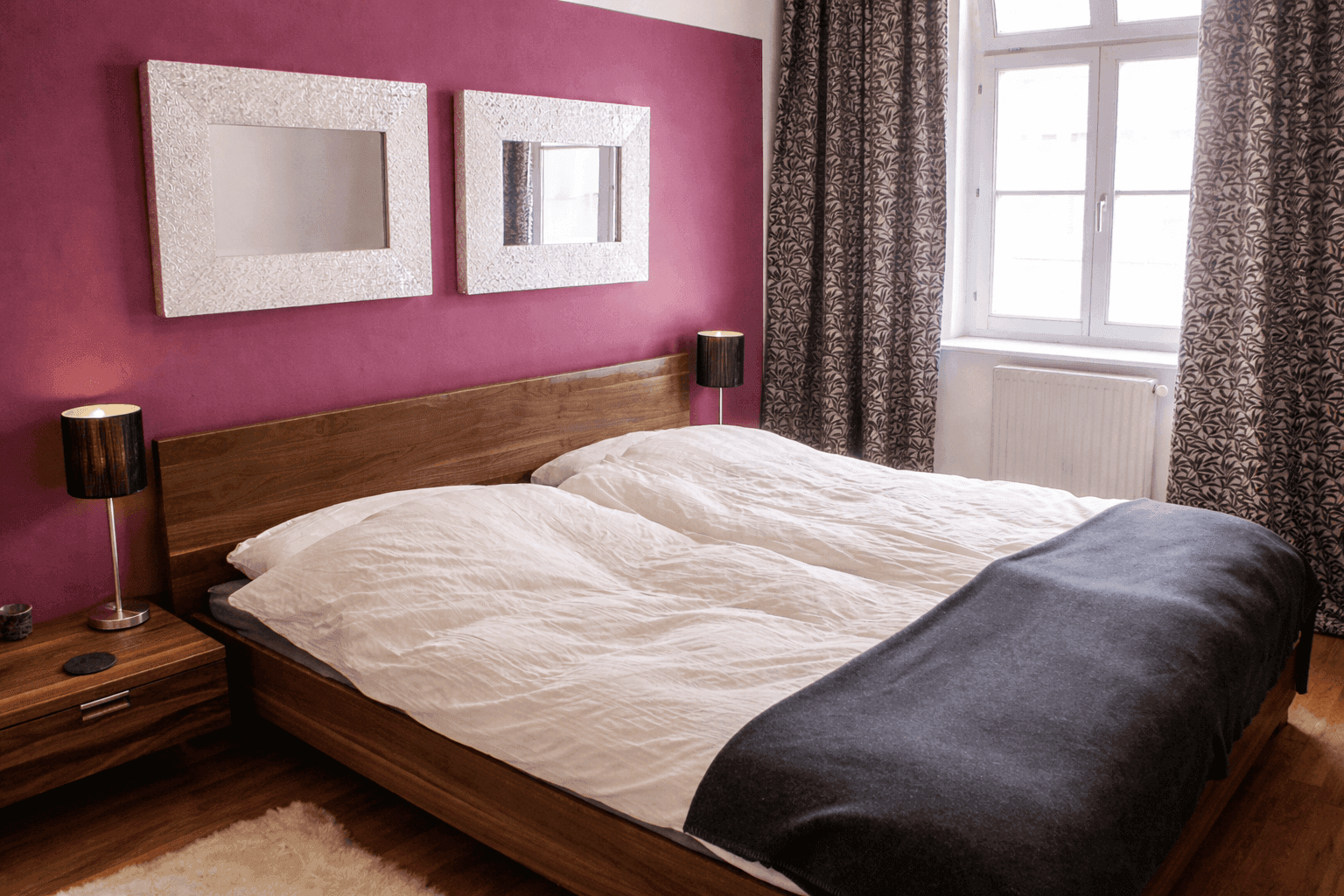 Schlafzimmer mit Holzbett, Nachttischen und einer auffälligen lila Akzentwand.