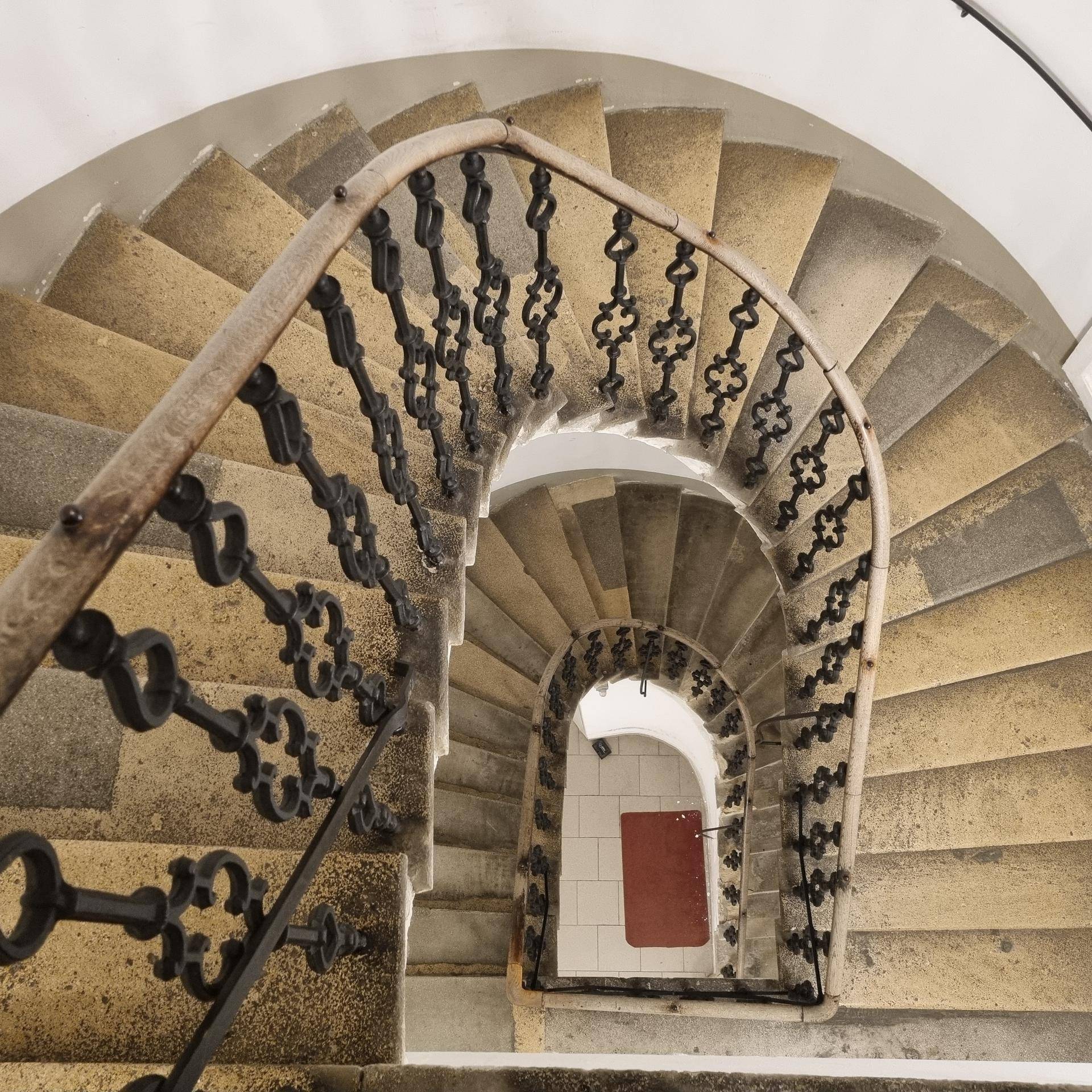 Elegante Wendeltreppe mit schmiedeeisernem Geländer in einem historischen Gebäude.
