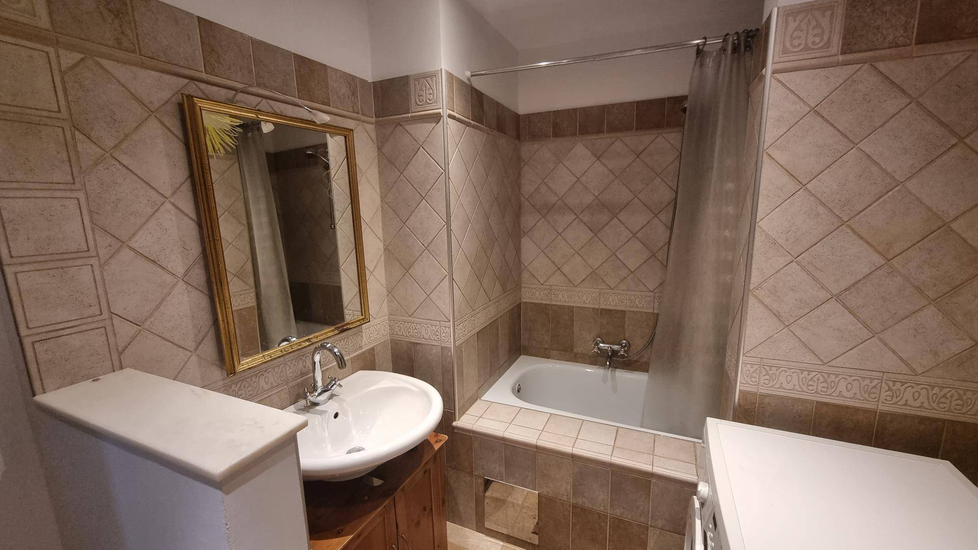 Badezimmer mit beigefarbenen Fliesen, Waschbecken, Spiegel und Badewanne mit Duschvorhang.