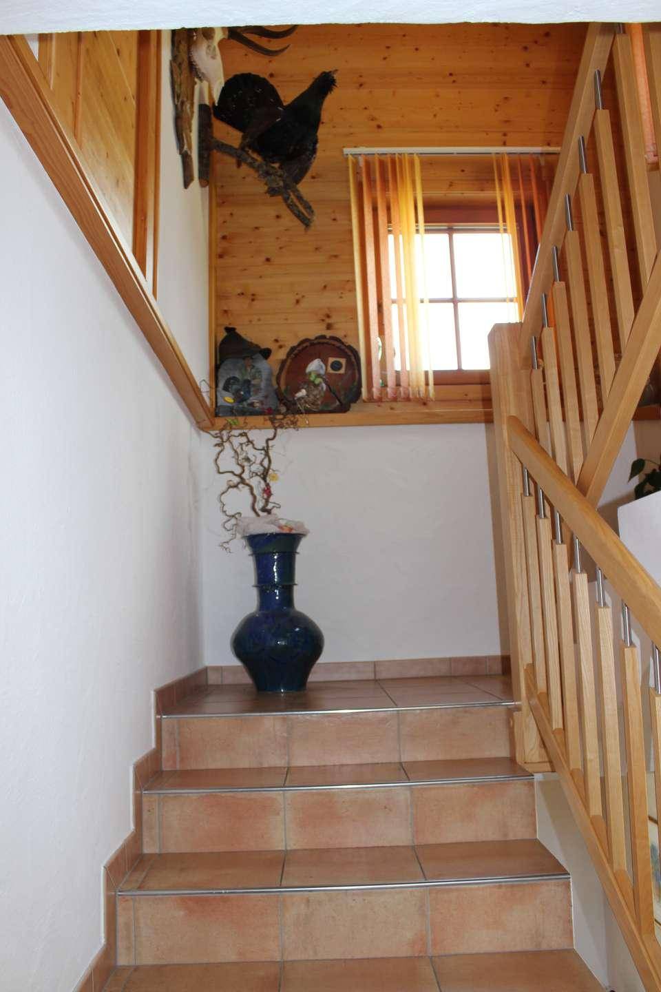 Treppenhaus mit gefliesten Stufen, Holzgeländer und holzvertäfelten Wänden im oberen Bereich.