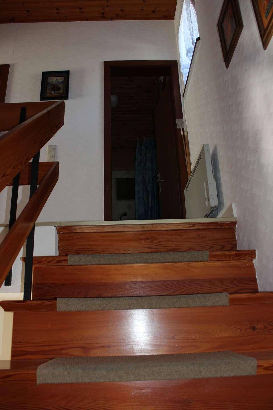 Holztreppe führt zu einem Raum mit Holzbalkendecke und einem Heizkörper an der Wand.