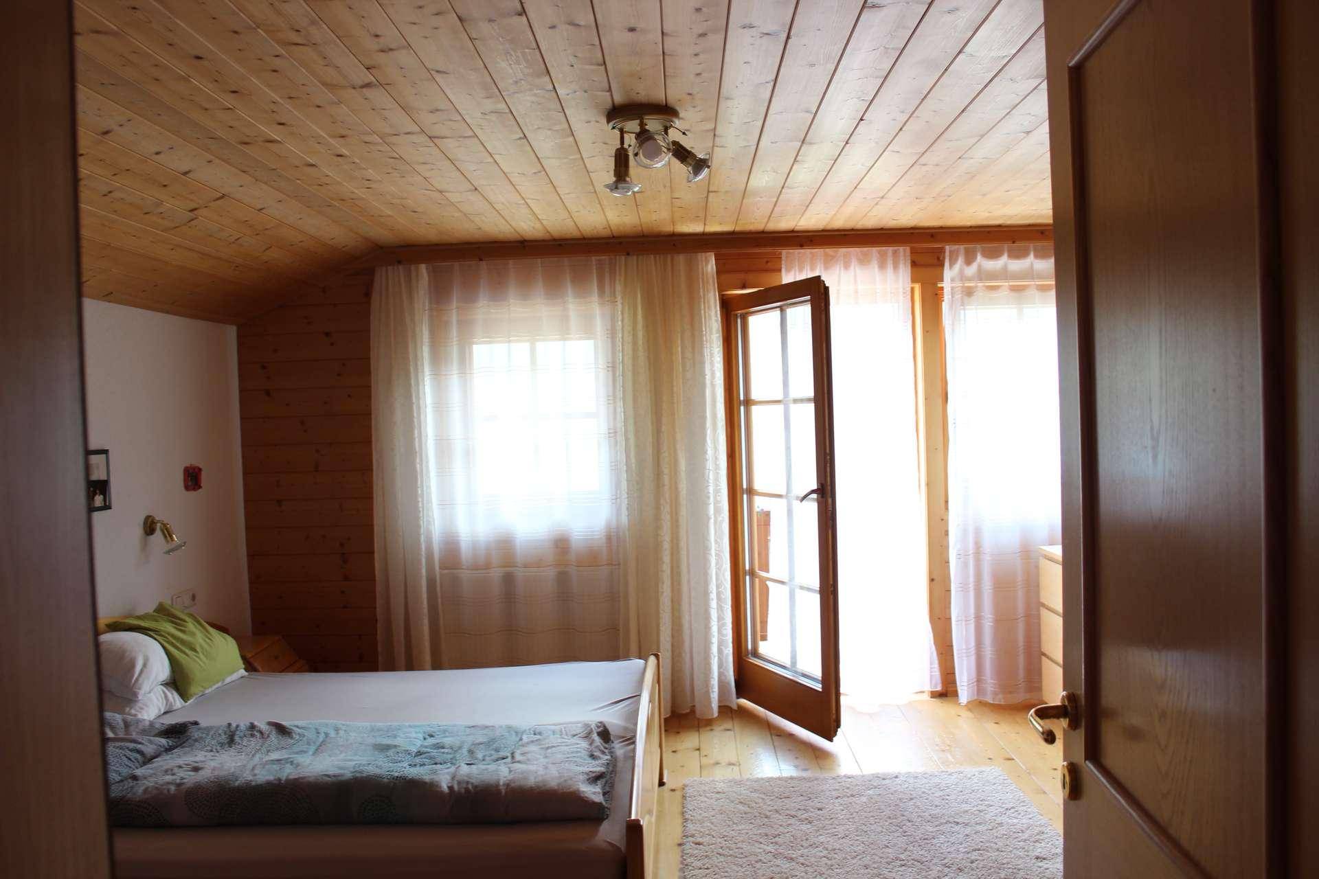 Gemütliches Schlafzimmer mit holzvertäfelten Wänden und Decke, viel Tageslicht und Zugang nach draußen.