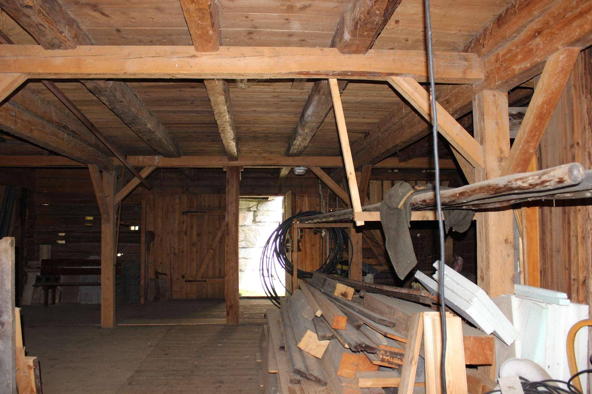 Rustikaler Innenraum eines alten Holzgebäudes mit sichtbaren Holzbalken und Dielenboden, gut erhalten.