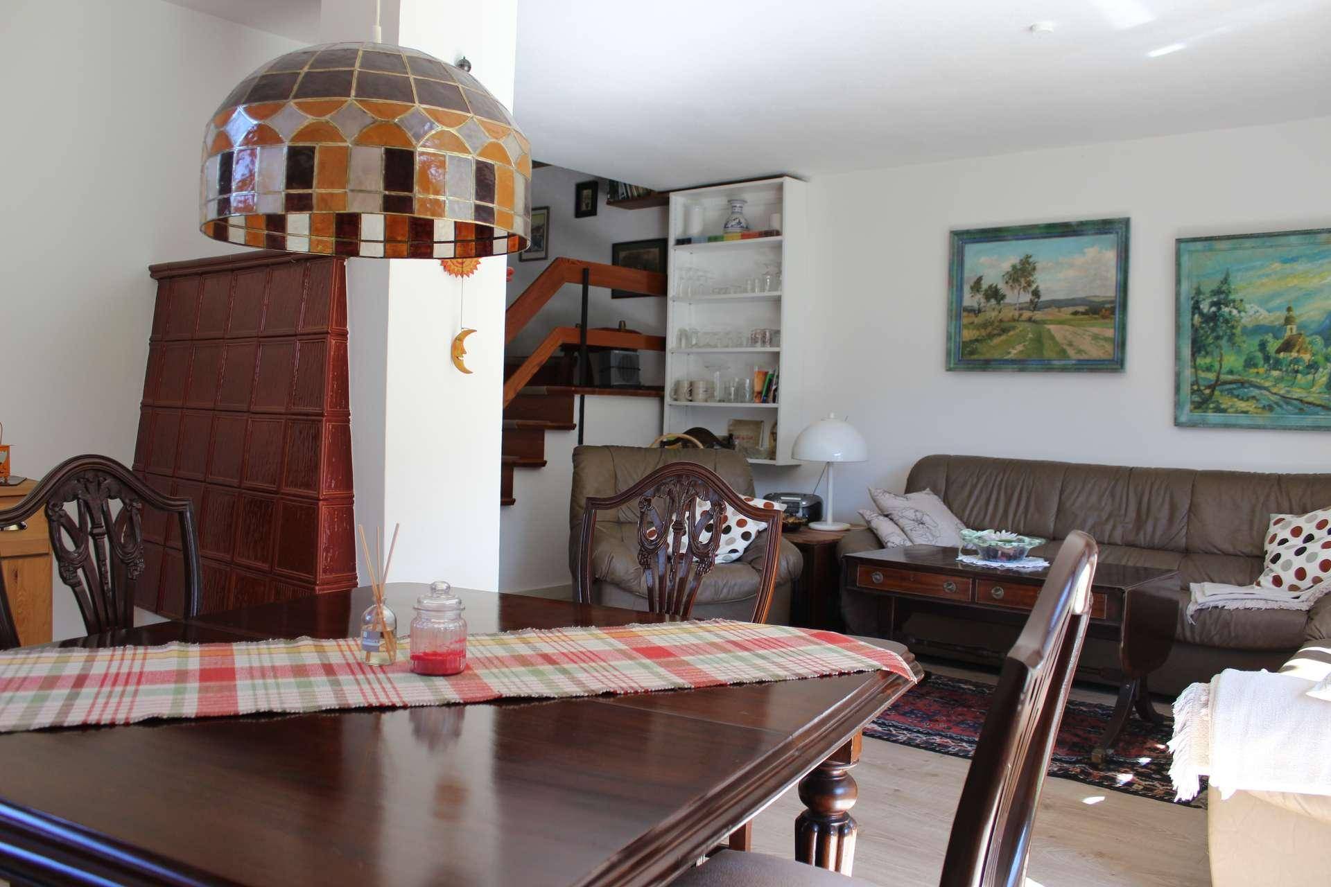 Gemütlicher Wohn-Essbereich mit traditionellem Kachelofen, Holztisch und Ledersofas.