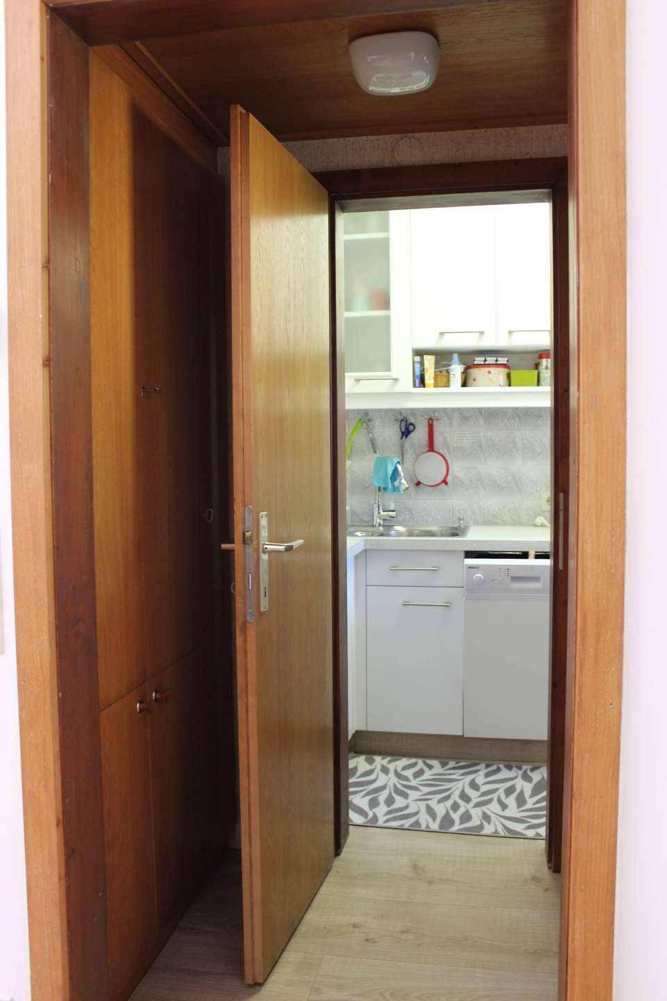 Blick durch eine Holztür in einen kleinen Hauswirtschaftsraum mit Spüle und Waschmaschine.
