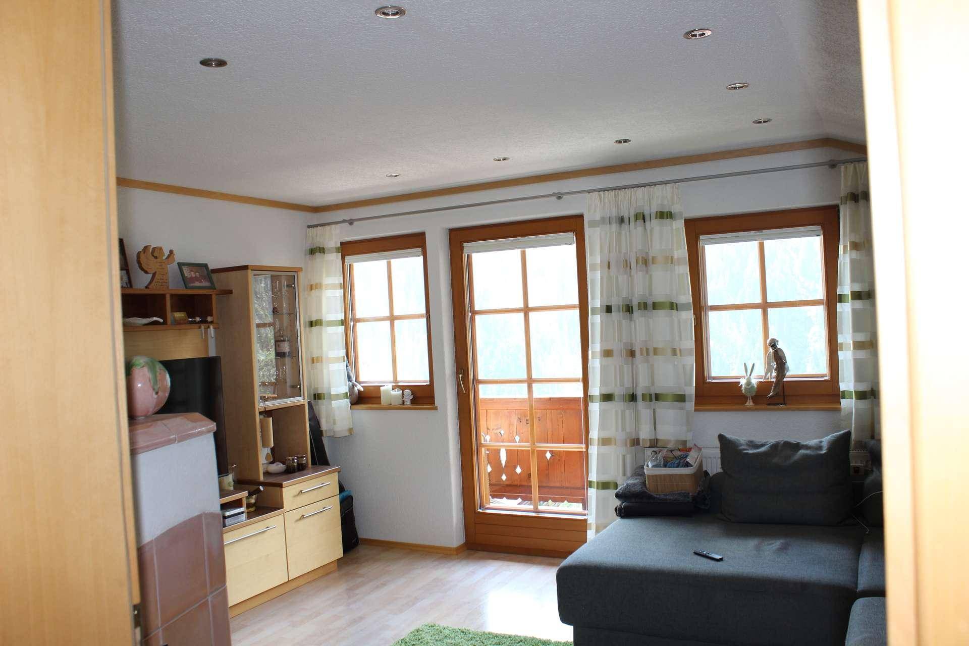 Wohnzimmer mit hellem Holzboden, einem dunkelgrauen Sofa und Fenstern mit Balkonzugang.