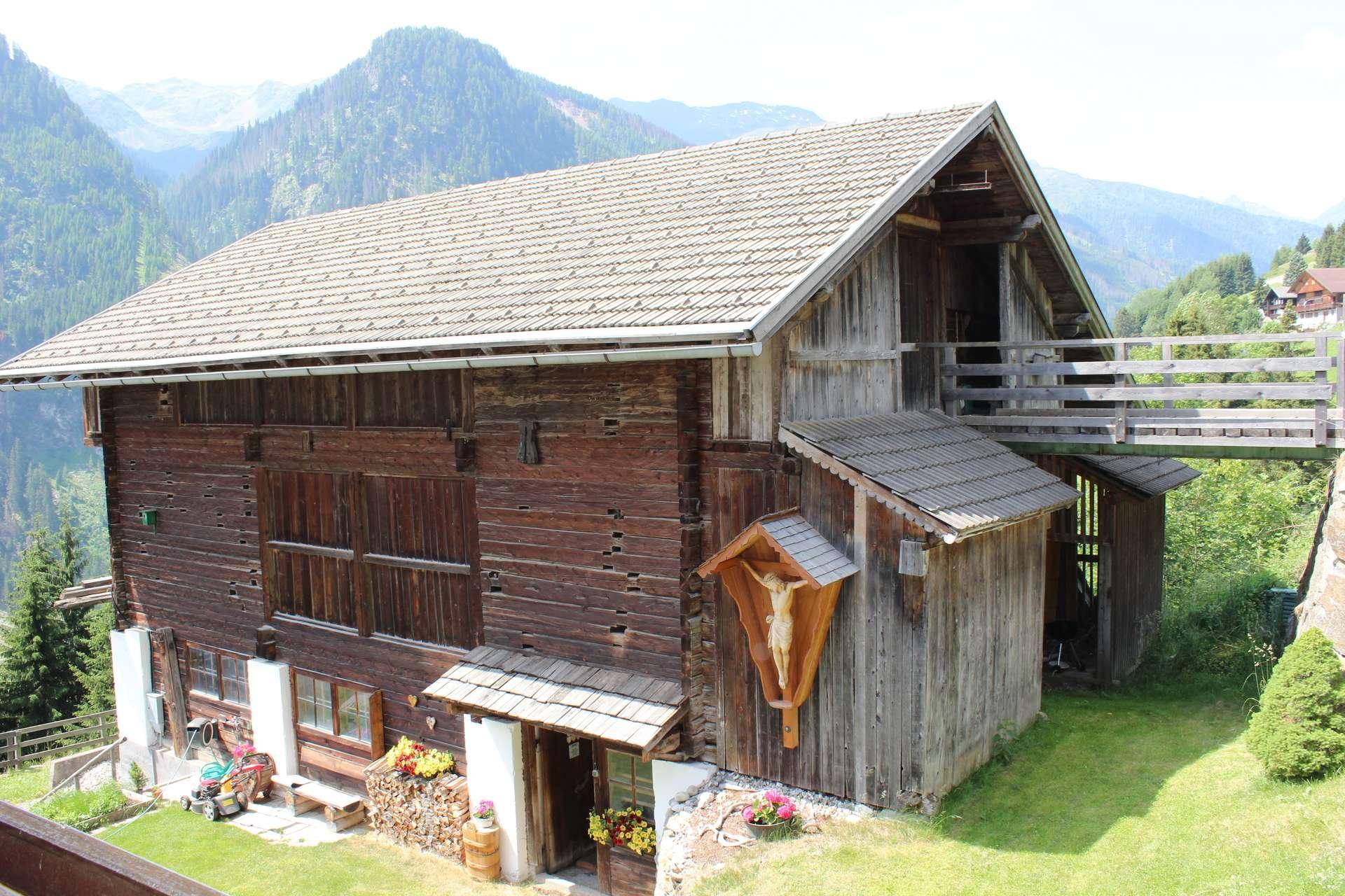 Altes, rustikales Holzgebäude mit traditioneller Kreuz-Dekoration, umgeben von grünen Wiesen und Bergen.