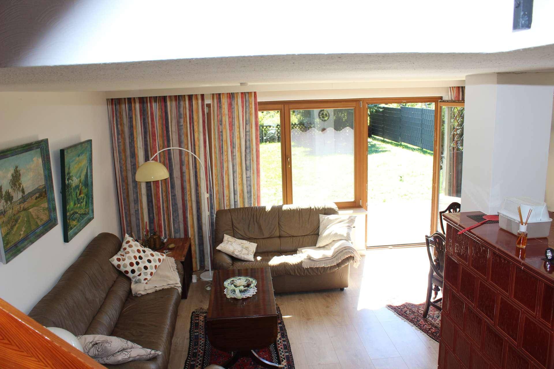 Helles Wohnzimmer mit Ledersofas, Holzboden und Zugang zum Garten durch große Fenster.