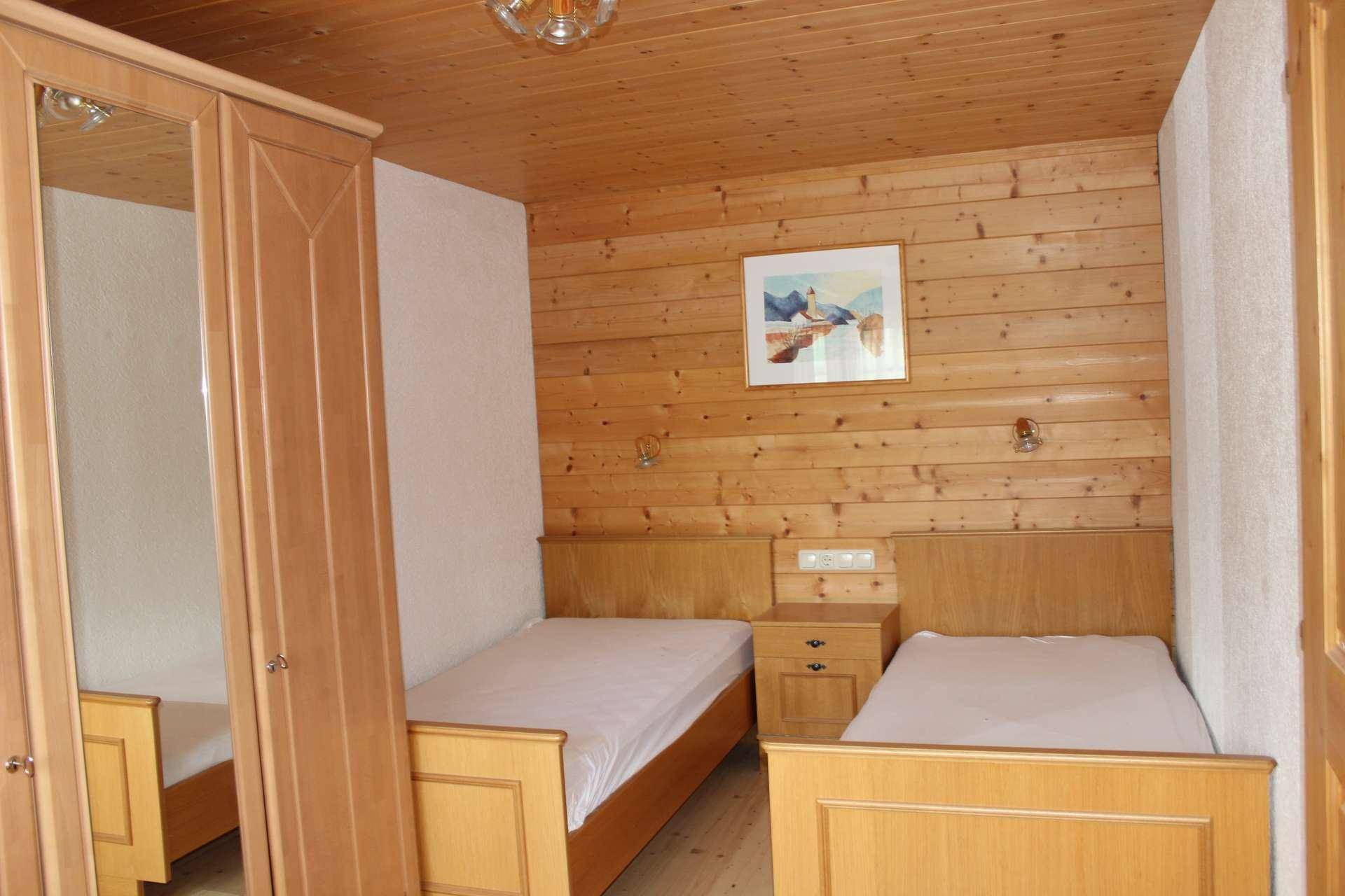 Schlafzimmer mit zwei Einzelbetten, holzvertäfelten Wänden und Decke sowie einem Holzschrank mit Spiegel.